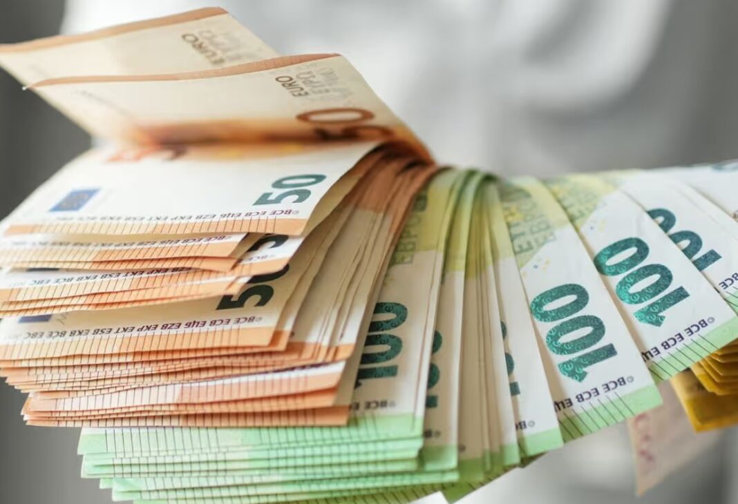 Fanned stack of euro banknotes with orange 50€ notes on top and green 100€ notes on the bottom held in a hand